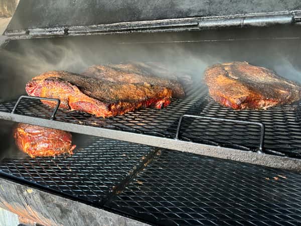 A close-up shot of brisket smoking in a smoker, with a rich bark forming on the meat and smoke swirling around.