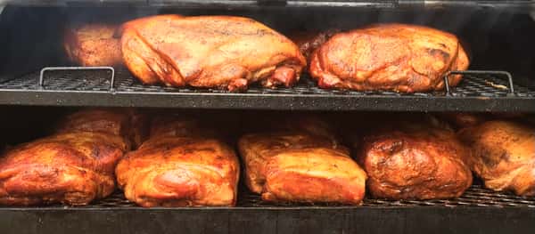 A smoker with multiple racks holding large cuts of meat being cooked, with some smoke rising from the top.