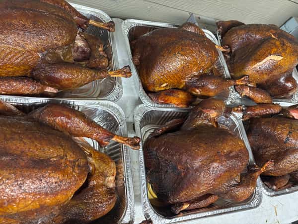 A tray filled with several perfectly smoked whole chickens, their skin crisped to a golden brown color.