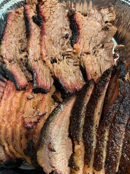 The image shows a close-up of slices of brisket with a well-browned, charred crust, and tender, juicy meat inside.