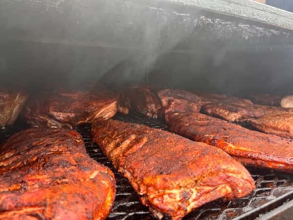 A smoky barbecue grill with several slabs of ribs cooking, showing a flavorful rub on the meat with some smoky mist rising around the grill.