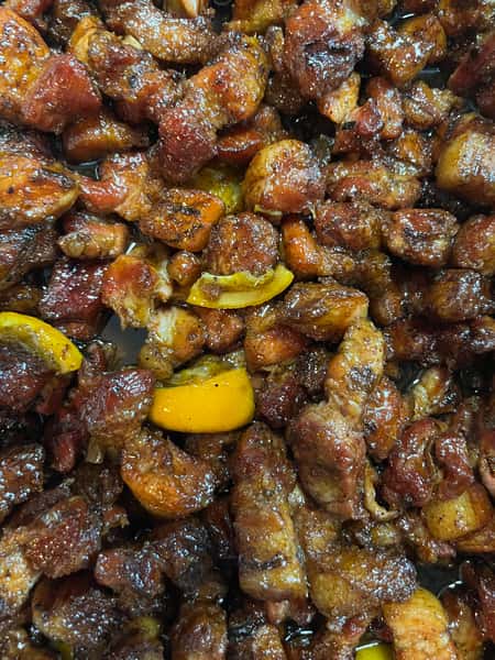 The image shows a close-up of a delicious dish with tender pieces of smoked or grilled meat coated in a dark, flavorful glaze. Some pieces of yellow pepper can be seen mixed in, adding a pop of color and hinting at a slightly tangy or spicy flavor. The meat appears crispy and caramelized from the cooking process.