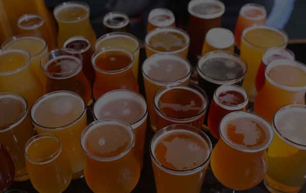 A vibrant assortment of craft beers in various styles and hues, ranging from pale golden ales to rich ambers and dark stouts, served in a mix of pint and tulip glasses—perfect for a brewery tasting flight or beer enthusiast's sampler.