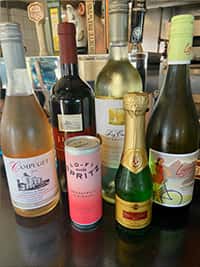 Assorted selection of wines and sparkling beverages displayed at The Riders Club Café, featuring red, white, and rosé varieties along with a canned spritz and mini champagne bottle, perfect for casual sipping or special occasions.