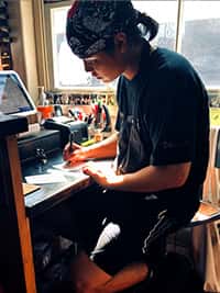 A focused staff member at The Riders Club Café working on paperwork near the register, with sunlight streaming through the window behind.