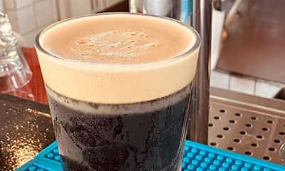 Close-up of a freshly poured pint of dark stout beer with a creamy head, served on a bar mat beside a chrome beer tap at The Riders Club CafƩ.