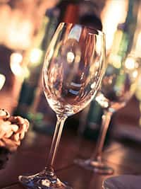 Close-up of an empty wine glass on a warmly lit wooden table, set against a blurred background of bottles and ambient bokeh lighting, evoking a cozy, upscale dining atmosphere.