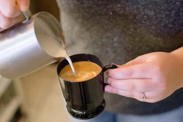 barista pouring cream into mug