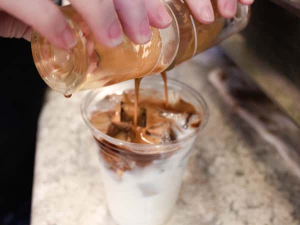 two shots of espresso being poured into an iced coffee