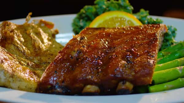 ribs and chicken on a plate with asparagus and lemon garnish