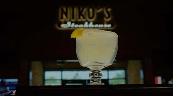 margarita with an orange garnish in front of a blurred, restaurant sign