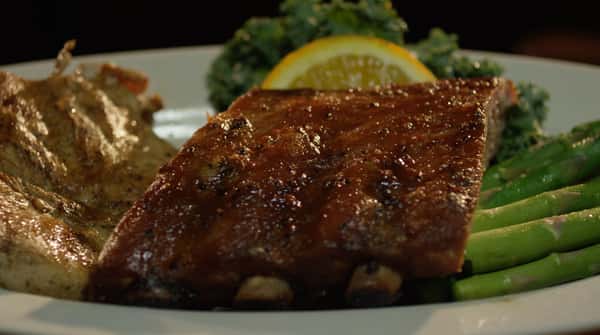 Ribs and chicken entree with aspargus and a lemon garnish on a plate