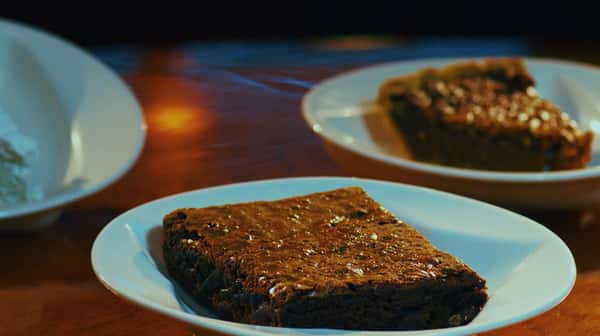 brownie on a plate with a piece of pie in the background