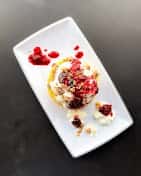 Plated gourmet dessert with creamy mousse or cheesecake topped with fresh berries, crushed nuts, and fruit coulis on a modern rectangular dish, styled for fine dining presentation