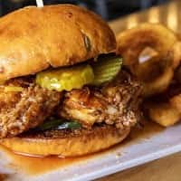 Crispy fried chicken sandwich with pickles and sauce on a soft brioche bun, paired with crunchy potato chips, showcasing a Southern-style comfort food meal