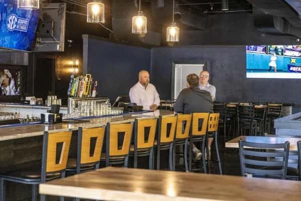 Modern sports bar interior with a sleek bar counter, draft beer taps, and guests enjoying drinks under warm pendant lighting, creating a lively casual dining atmosphere