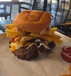 Loaded cheeseburger with melted cheddar, crispy onion rings, and a thick beef patty on a toasted bun, served with fries and ketchup in a casual restaurant setting