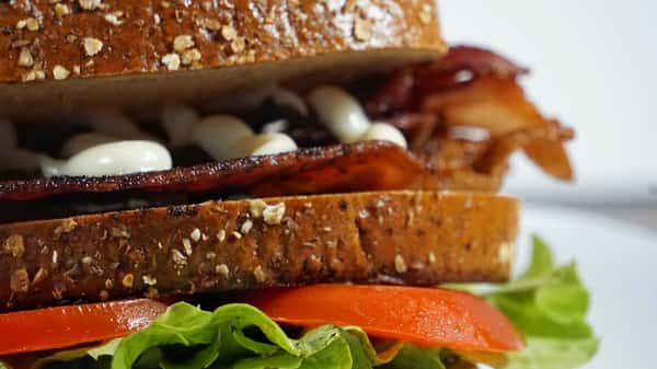 Close-up of a BLT sandwich on multigrain bread with crispy bacon, lettuce, tomato, and drizzled mayonnaise.