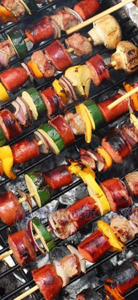 Grilled kabobs with sausage, beef, zucchini, peppers, onions, and mushrooms cooking over hot charcoal.