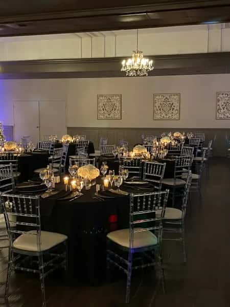 Elegant banquet hall with black tablecloths, clear chairs, candlelit centerpieces, and chandeliers creating a warm, formal ambiance.