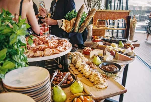 Lavish charcuterie spread with cured meats, cheeses, bread, pears, olives, dips, and fresh herbs set up for a catered event.