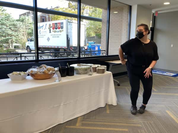 Catering setup with covered food bowls on a white tablecloth, a staff member in black nearby, and a Robert J Events & Catering truck outside.