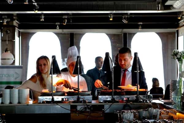 Guests being served freshly prepared food by a chef at a buffet station during a catered event in a modern venue.