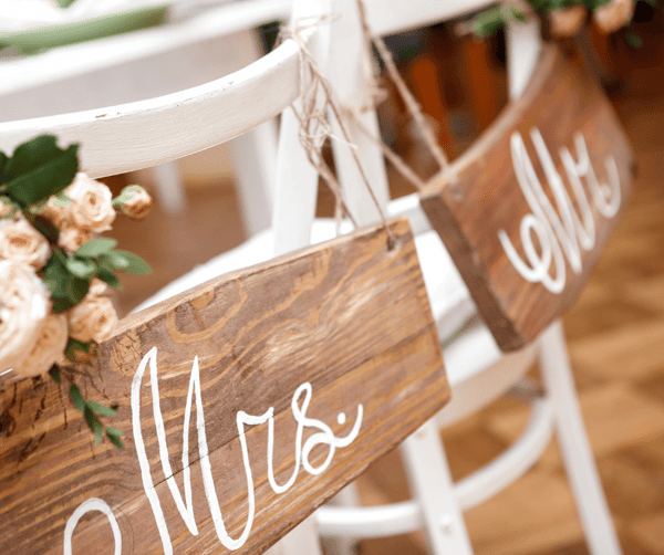 Rustic wooden "Mr." and "Mrs." signs tied to white wedding chairs decorated with blush roses and greenery.