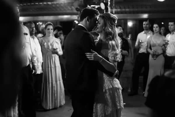 Bride and groom share a romantic first dance surrounded by guests in an intimate black and white wedding scene.