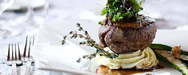 Gourmet filet mignon served on mashed potatoes with asparagus, microgreens, thyme garnish, and rich brown sauce.