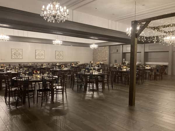 Elegant banquet hall with round tables set for an event, chandeliers overhead, and warm lighting highlighting floral centerpieces.