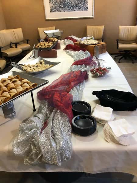 Catering table with assorted pastries, appetizers, and fruit, decorated with silver and red fabric, set in a conference room.
