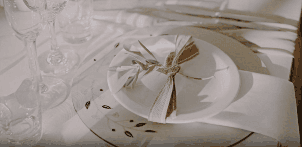 Elegant table setting with white plates, a rustic burlap ribbon, olive branch detail, and glassware for a refined dining experience.