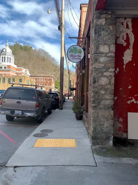 A street view of a brick building with a "Mad Co Brewing" sign. The brewery is located in a charming town, with a courthouse visible in the distance.