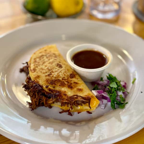 Quesabirria Taco With Consume on the side, garnished with red onion & Cilantro.
