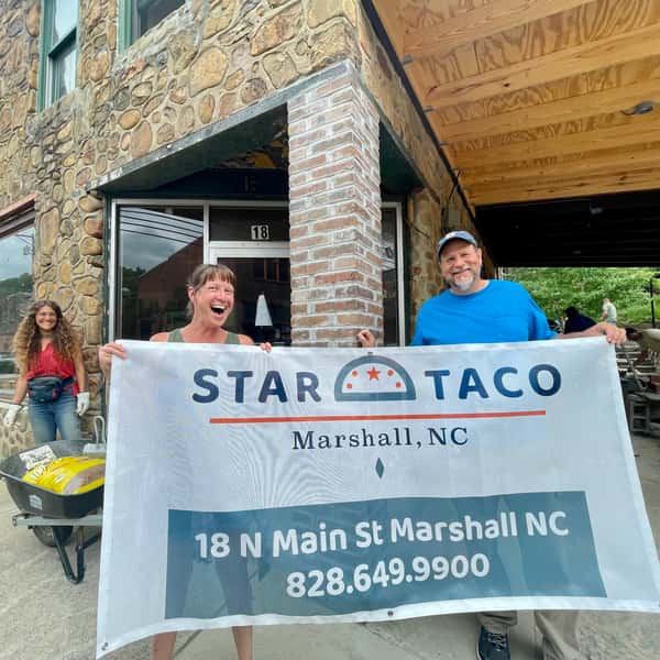 Kate & Brian holding a Banner that says "Star Taco" in front of a building under construction