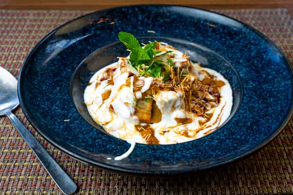 Dahi papdi chaat — crispy papdi topped with yogurt, tamarind chutney, sev, herbs, and mint garnish on a blue plate.