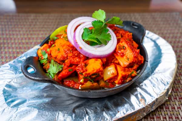 Kadai paneer — spiced paneer stir-fry with bell peppers, onions, and tomatoes served in a sizzling skillet with fresh cilantro and onion rings.