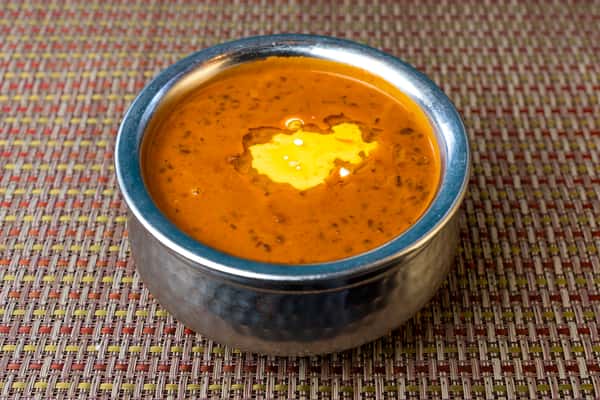 Dal makhani — slow-cooked black lentils in a rich buttery tomato gravy, finished with melted butter in a traditional metal bowl.