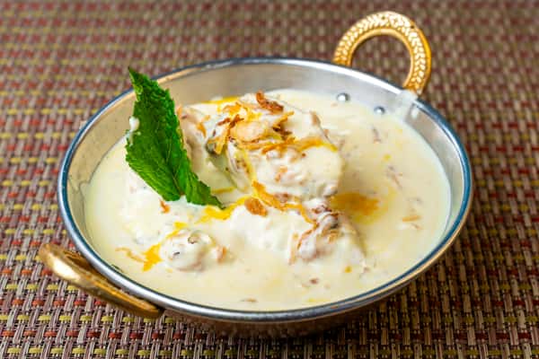 Malai kofta in a creamy white gravy topped with fried onions and mint, served in a traditional Indian metal bowl—rich vegetarian curry with soft dumpling koftas.