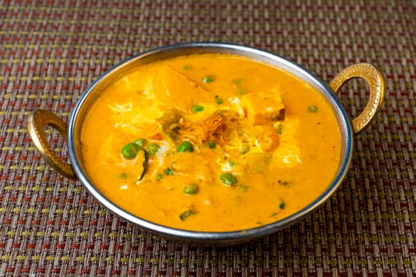 Paneer butter masala with green peas in a creamy tomato and cream gravy, served in a classic Indian karahi dish.