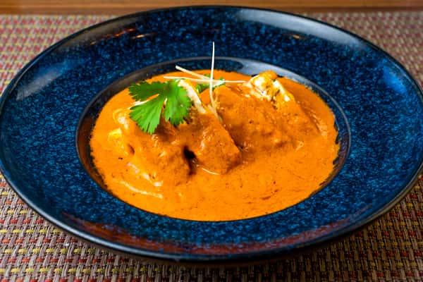 Paneer butter masala — soft paneer cubes in a rich creamy tomato gravy, garnished with cilantro and ginger on a blue plate.