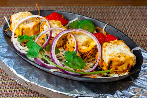 Paneer tikka cubes grilled and served on a sizzling platter with cabbage, red onions, cilantro, and bell peppers.