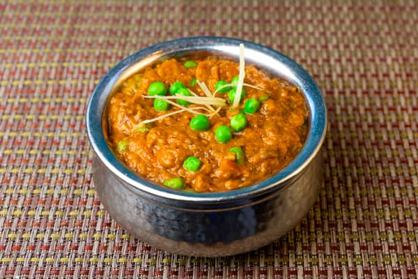 Matar paneer curry with green peas in a creamy tomato-based gravy, garnished with julienned ginger in a traditional metal bowl.