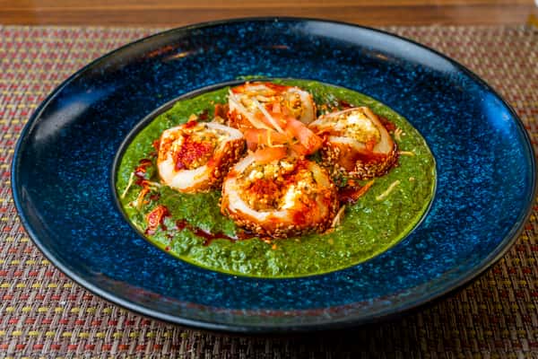 Sesame-crusted stuffed eggs served over creamy spinach sauce, topped with chili oil, sesame seeds, and shredded vegetables — Indo-fusion egg appetizer on a vibrant blue plate.