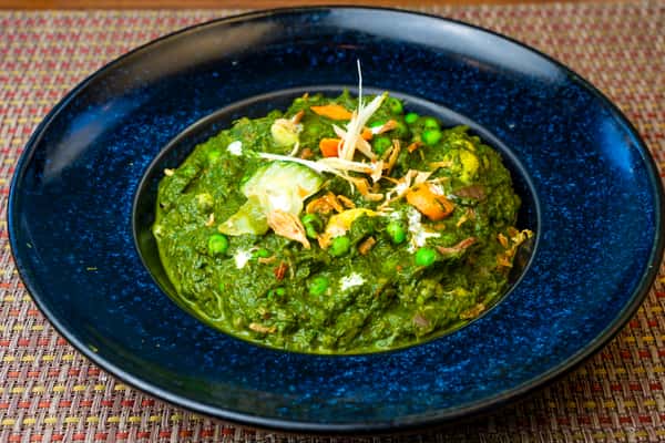 Creamy palak paneer with green peas and paneer cubes in a rich spinach gravy, topped with ginger and crispy onions on a blue plate.