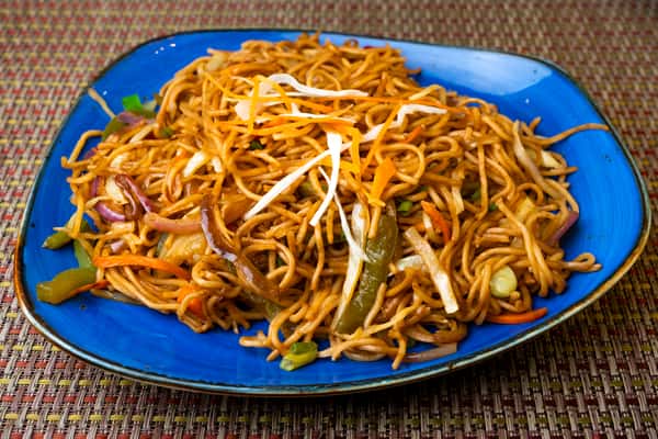 Indo-Chinese vegetable chow mein — stir-fried noodles with cabbage, carrots, peppers, and onions on a blue plate.