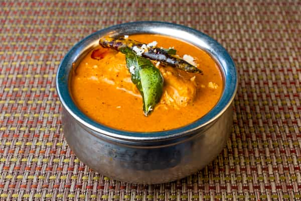 Creamy South Indian coconut curry with chicken, garnished with curry leaves and dried chili, served in a traditional metal bowl.
