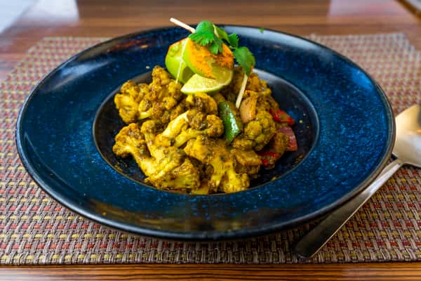 Spiced cauliflower stir-fry with peppers, herbs, and lime garnish on a blue plate — flavorful Indian gobi masala style dish.
