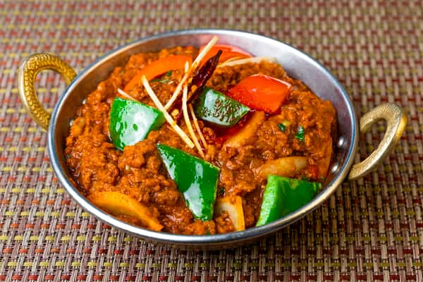 Spicy Indo-Chinese chili chicken in thick brown gravy with bell peppers, onions, and ginger garnish, served in a traditional metal karahi bowl.